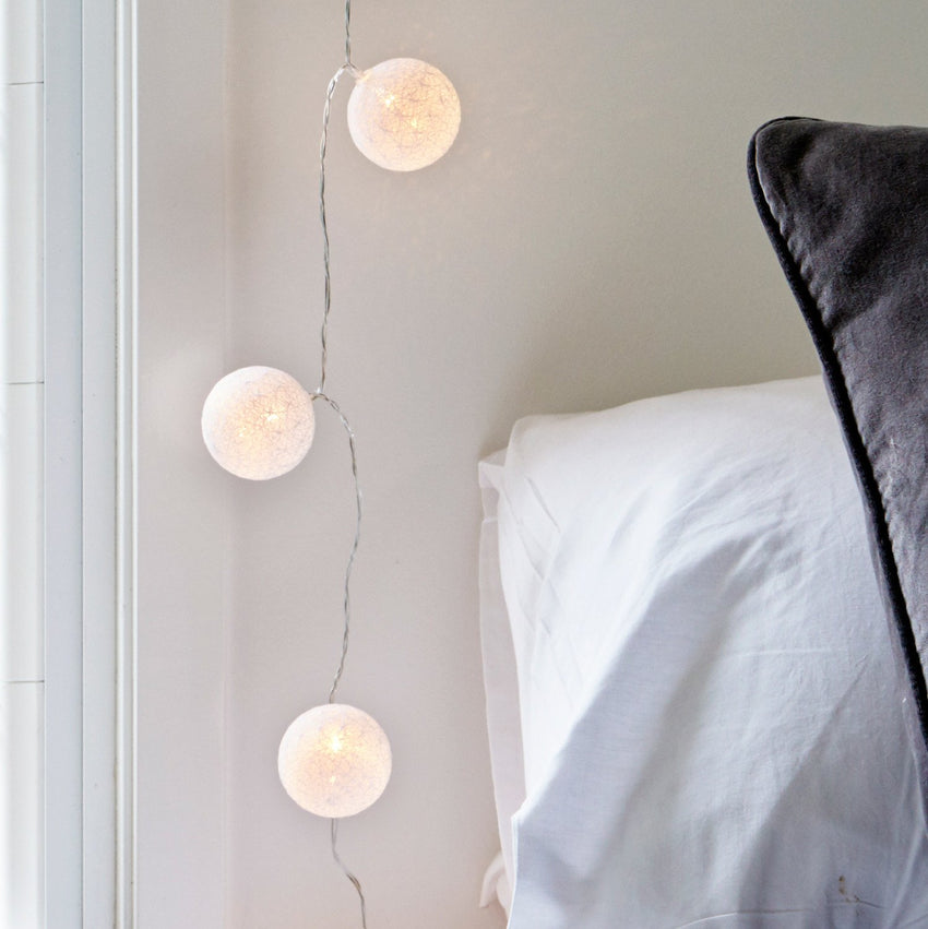 Lichterkette mit weißen Stoffbällen an der Wand neben einem Bett