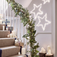 Mit LED Kerzen, LED Weihnachtsbaumkugeln, LED Sternen, Girlande und Geschenken dekorierte weiße Holztreppe mit Treppenläufer