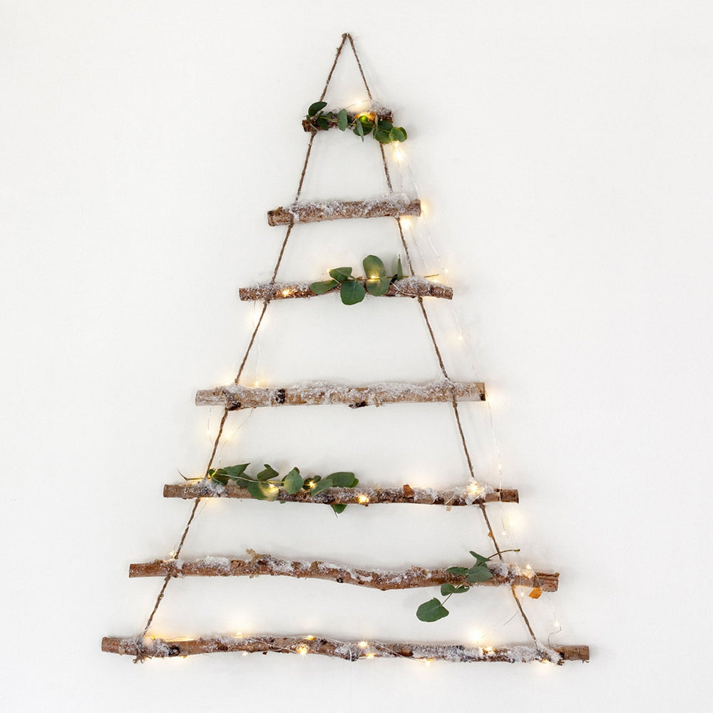 Birkenbaum Weihnachtsdeko aus Ästen mit Glitzer-Kunstschnee und Lichterkette an weißer Wand