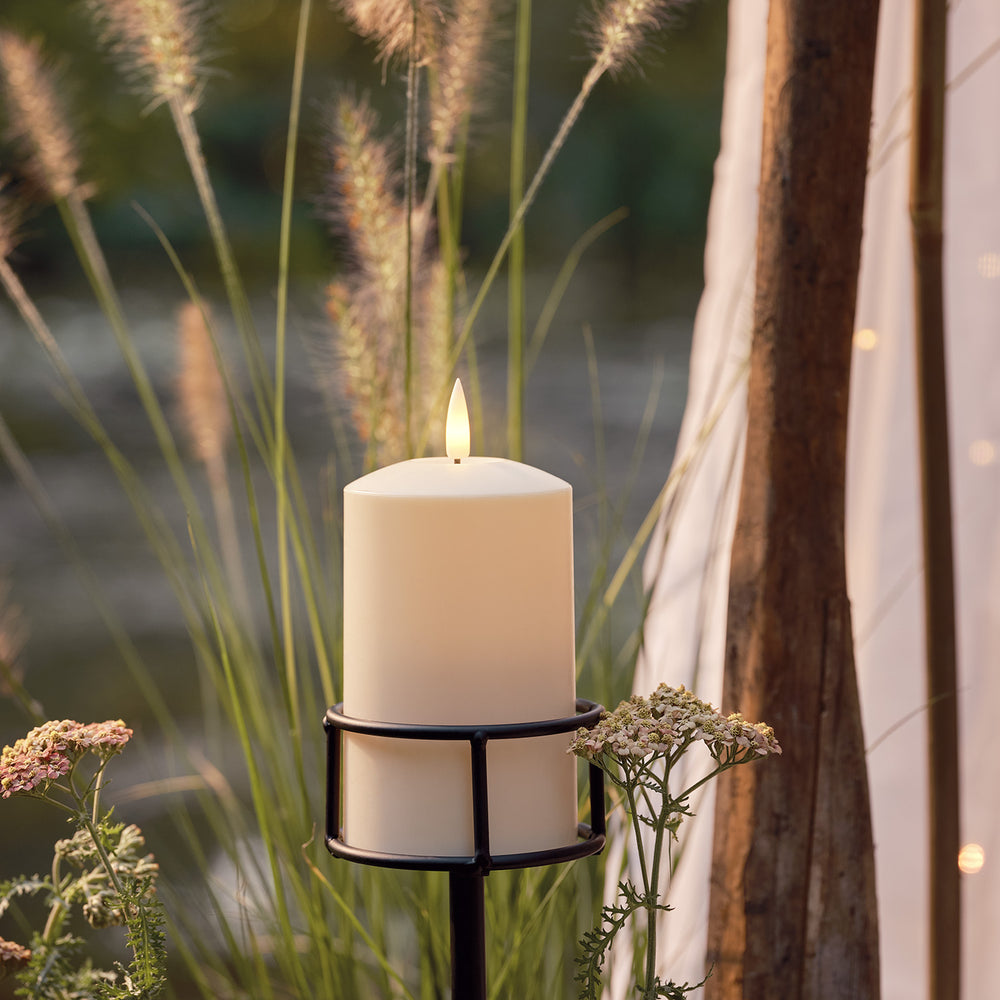 LED-Stumpenkerze in schwarzem Metall-Kerzenhalter im Garten mit Gräsern und Blumen