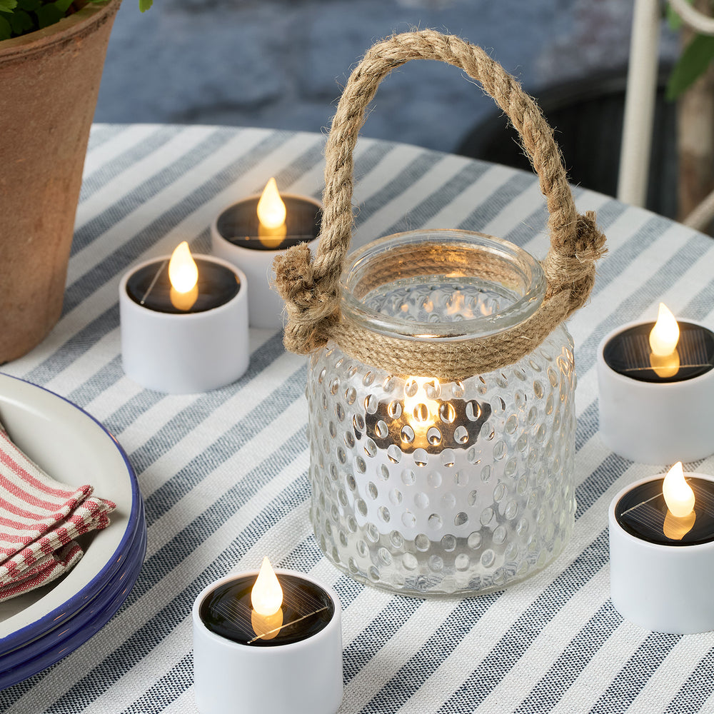 Solar LED Teelichter um eine Glaslaterne mit Juteband auf gestreiftem Tisch