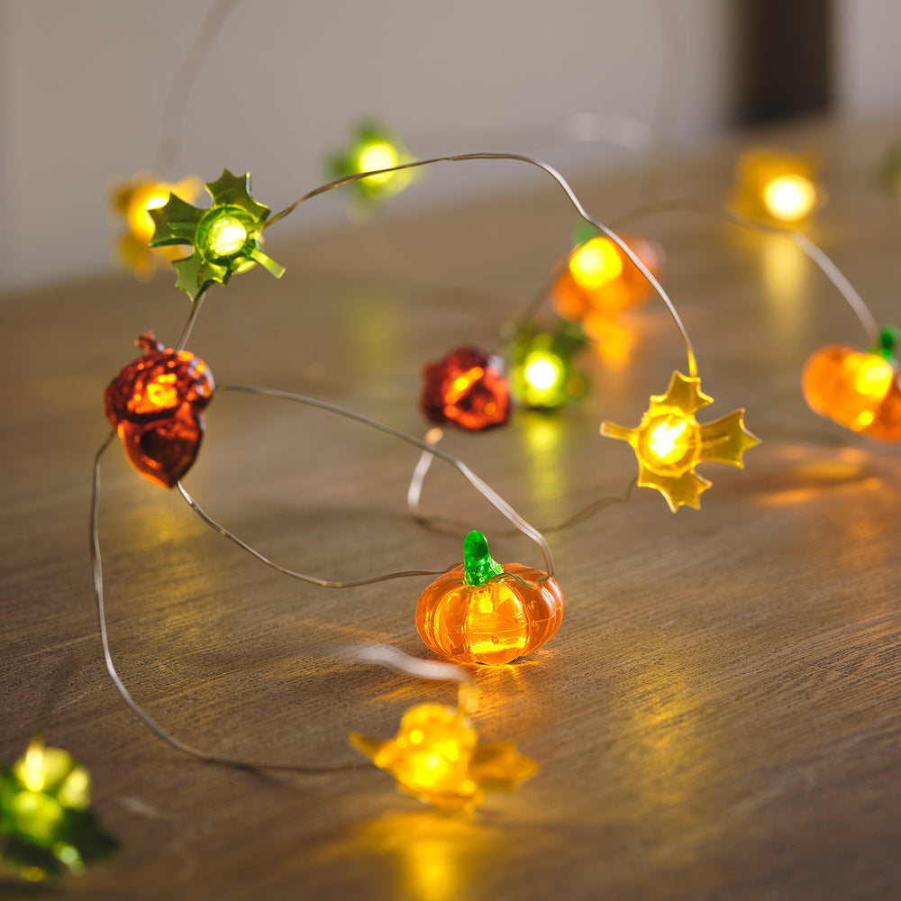 Herbstliche Lichterkette mit leuchtenden Kürbissen, Eicheln und Ahornblättern auf Holzoberfläche