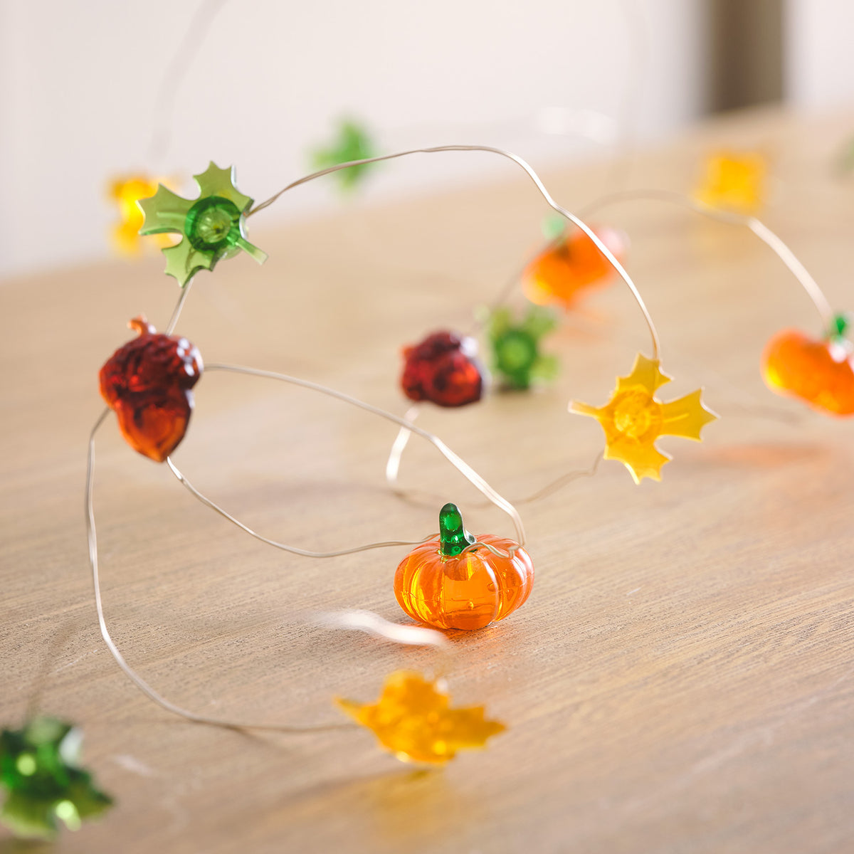 Herbstliche Lichterkette mit Kürbissen, Eicheln und Ahornblättern auf Holzuntergrund