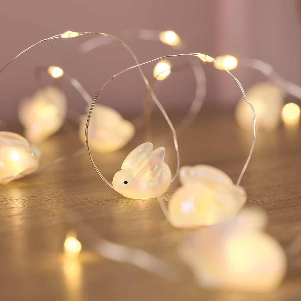 Nahaufnahme einer LED-Lichterkette mit kleinen, leuchtenden Hasenfiguren auf Holzuntergrund