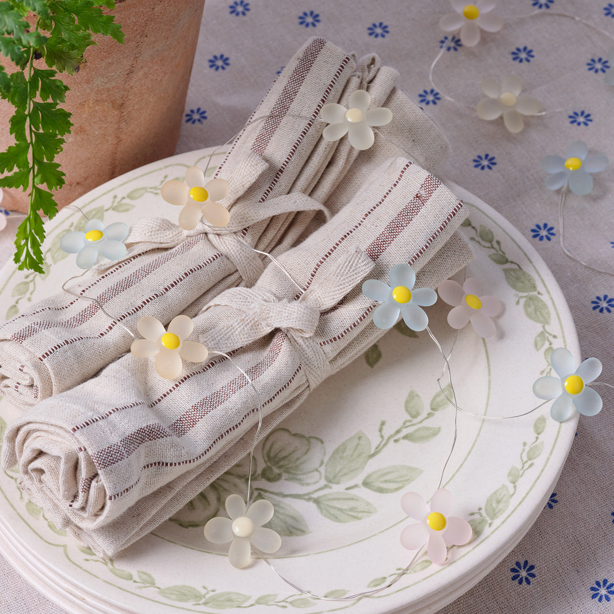 LED-Gänseblümchen-Lichterkette mit weißen und pastellfarbenen Blumen auf Teller mit Servietten
