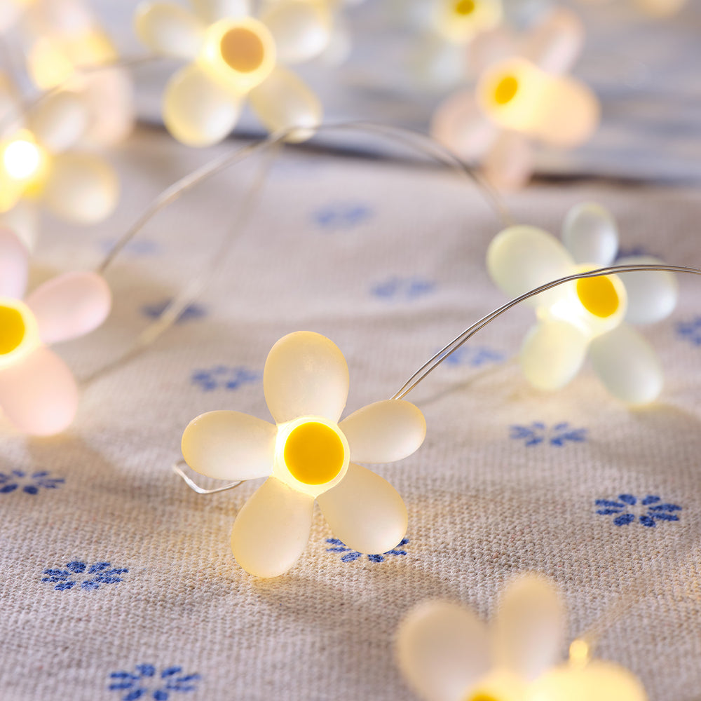 Nahaufnahme einer LED-Lichterkette mit weißen Gänseblümchen auf Stoff mit blauen Blumenmuster