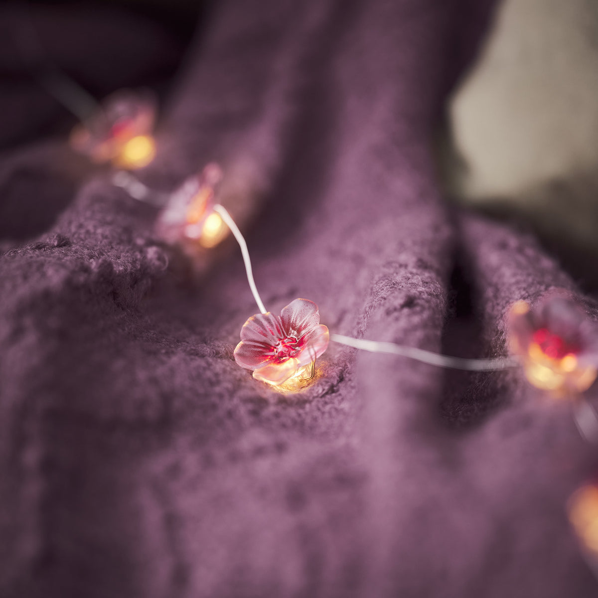 Lichterkette mit pinken Kirschblüten auf lila Strickdecke und Kissen drapiert