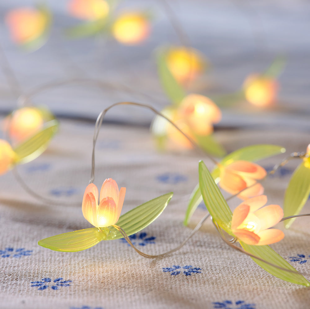 Nahaufnahme der LED-Lichterkette mit gelben Blüten auf hellgrauem Stoff mit blauen Blumenmotiven