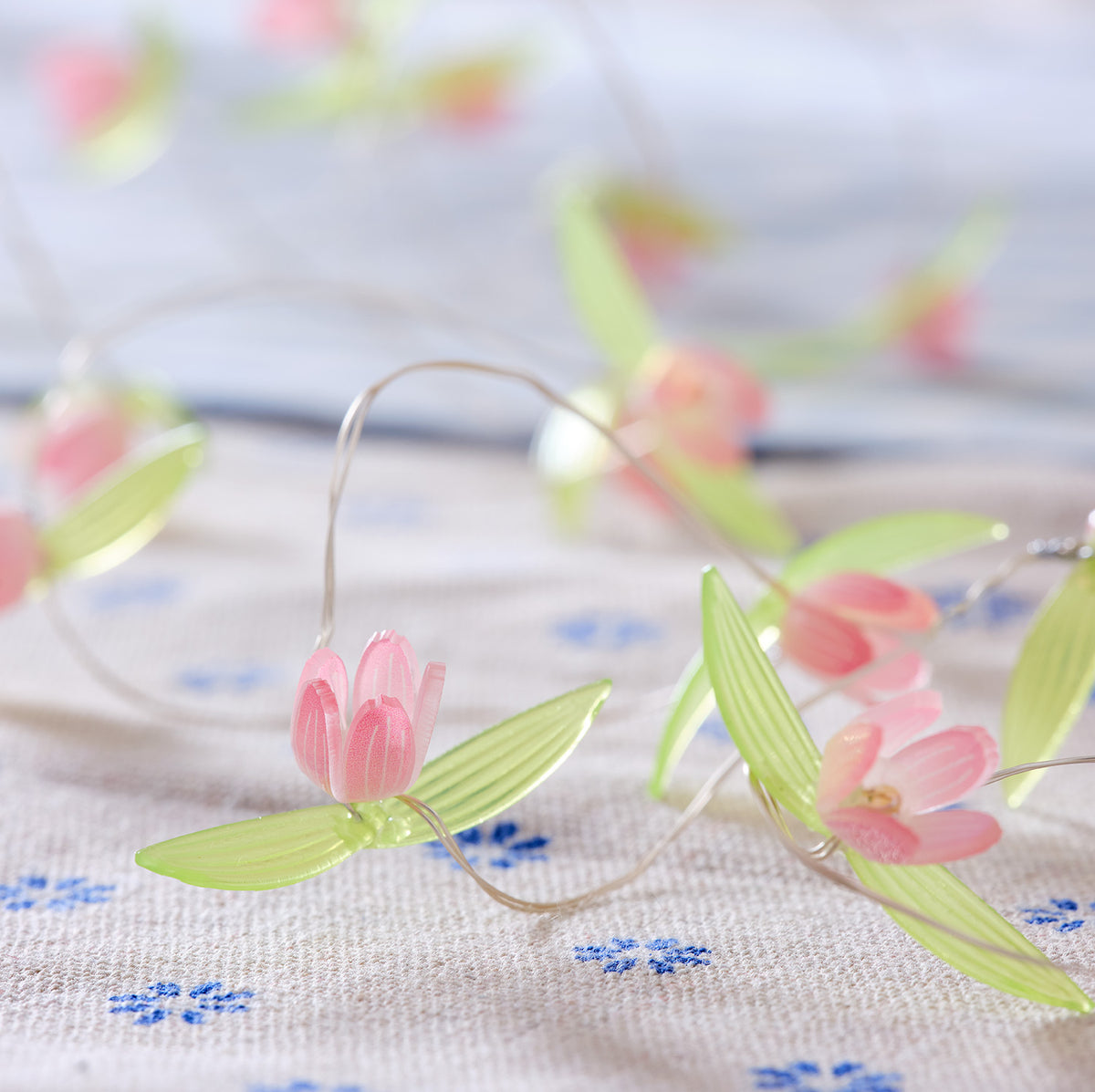 Nahaufnahme der LED-Lichterkette mit pinken Blüten auf hellgrauem Stoff mit blauen Blumenmotiven