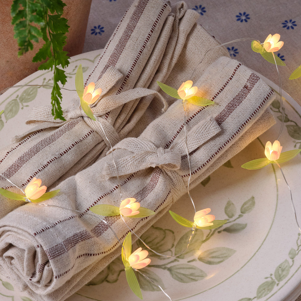 Warmweiße LED-Lichterkette mit kleinen gelben Blüten auf beige-weiß gestreiften Stoffservietten