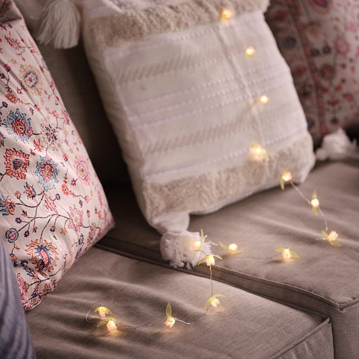 LED-Lichterkette mit kleinen gelben Blüten dekorativ auf Sofa mit Kissen drapiert