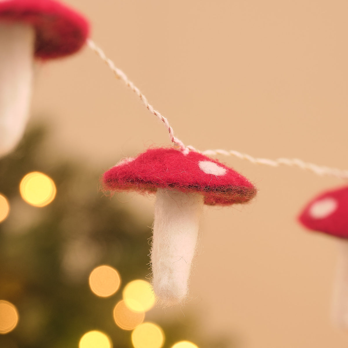 Detailaufnahme eines Filz-Fliegenpilzes an einer LED-Lichterkette, roter gepunkteter Hut, weißer Stiel, Lichterkettenfaden im Hintergrund.