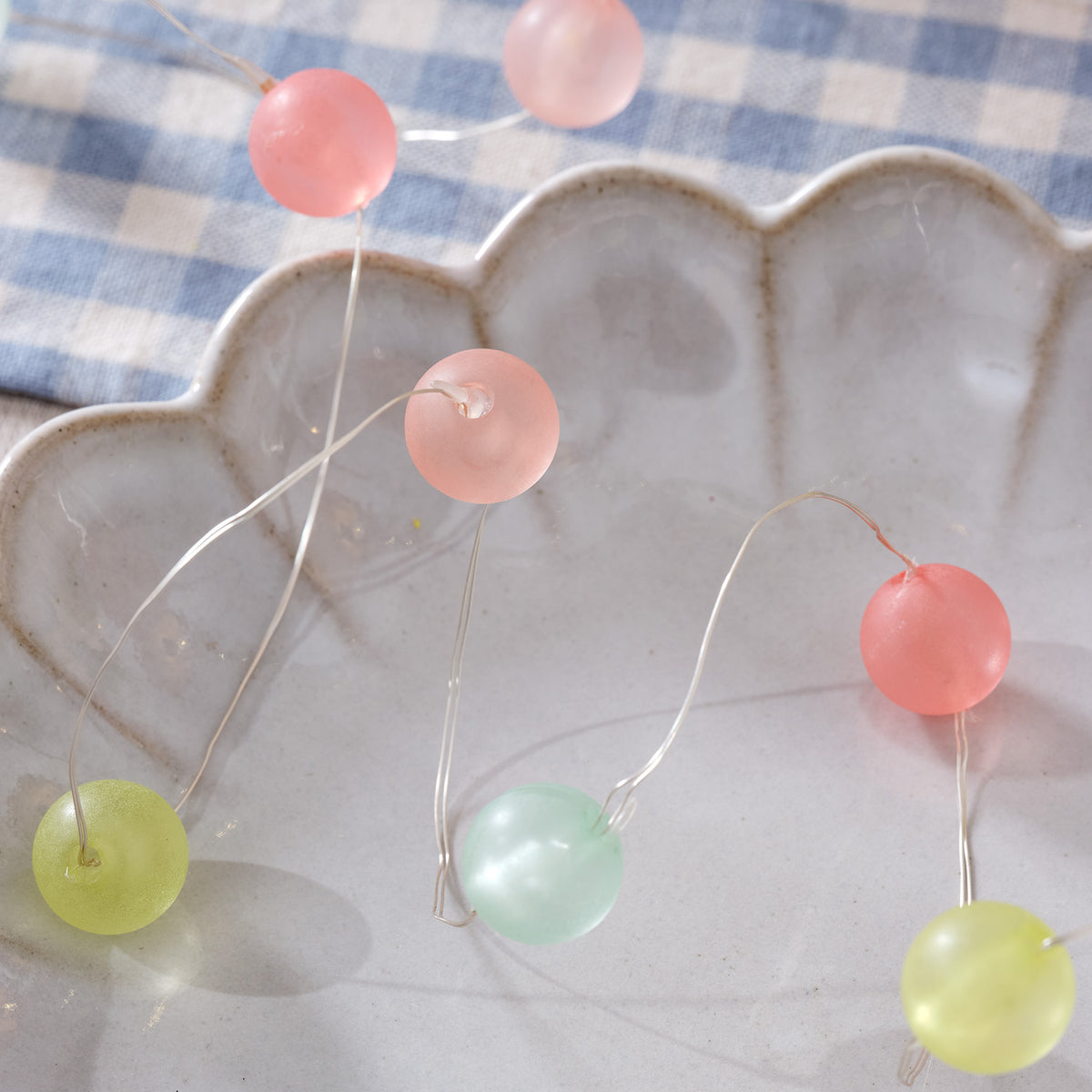 LED Lichterkette mit pastellfarbenen Kugeln auf grauer Muschel-Schale und blau kariertem Stoff