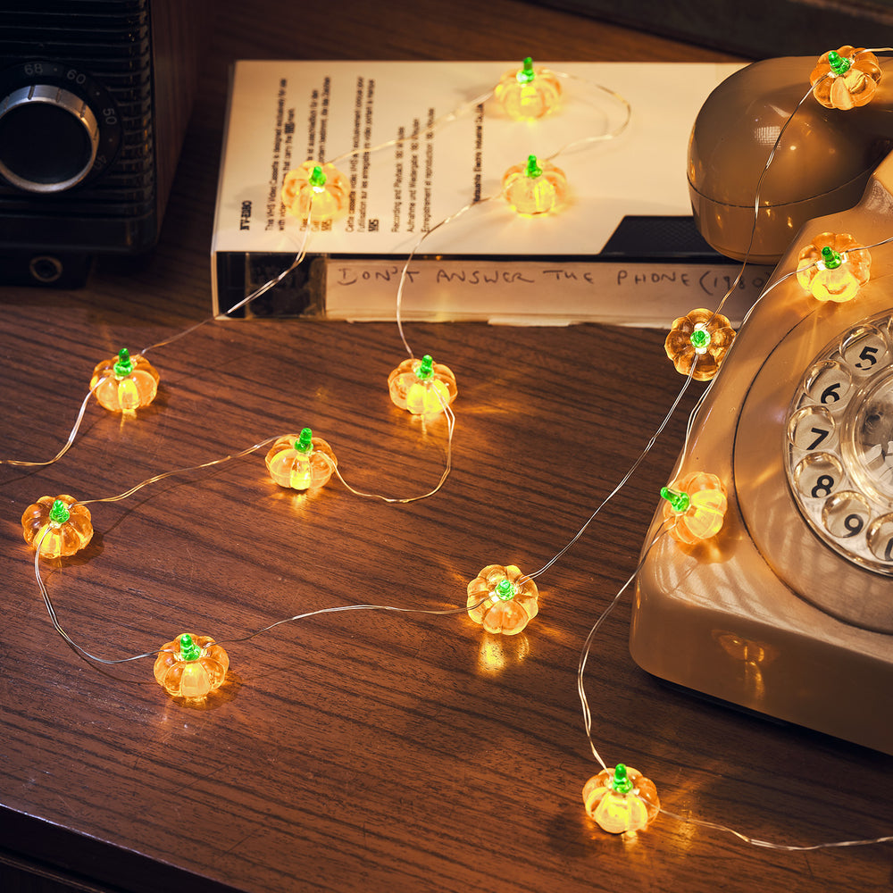 Leuchtende Kürbis-Lichterkette auf Holztisch neben altem Telefon und Kassette