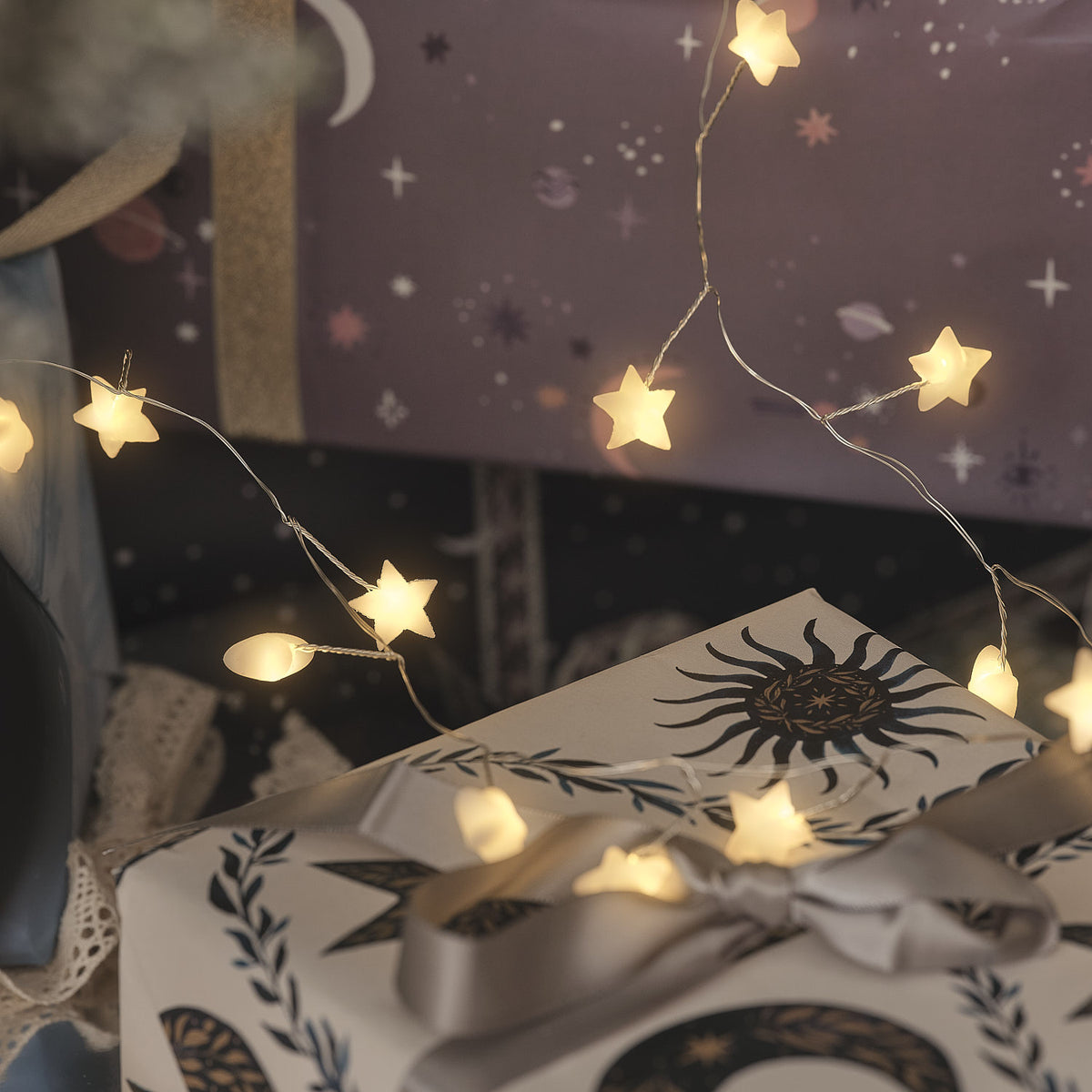 Weiße Stern-LED-Lichterkette in festlicher Weihnachtsdekoration mit Geschenkboxen, Kerzen und Weihnachtskugeln, warmweiße Lichter in elegant gestalteter Wohn-Inszenierung.