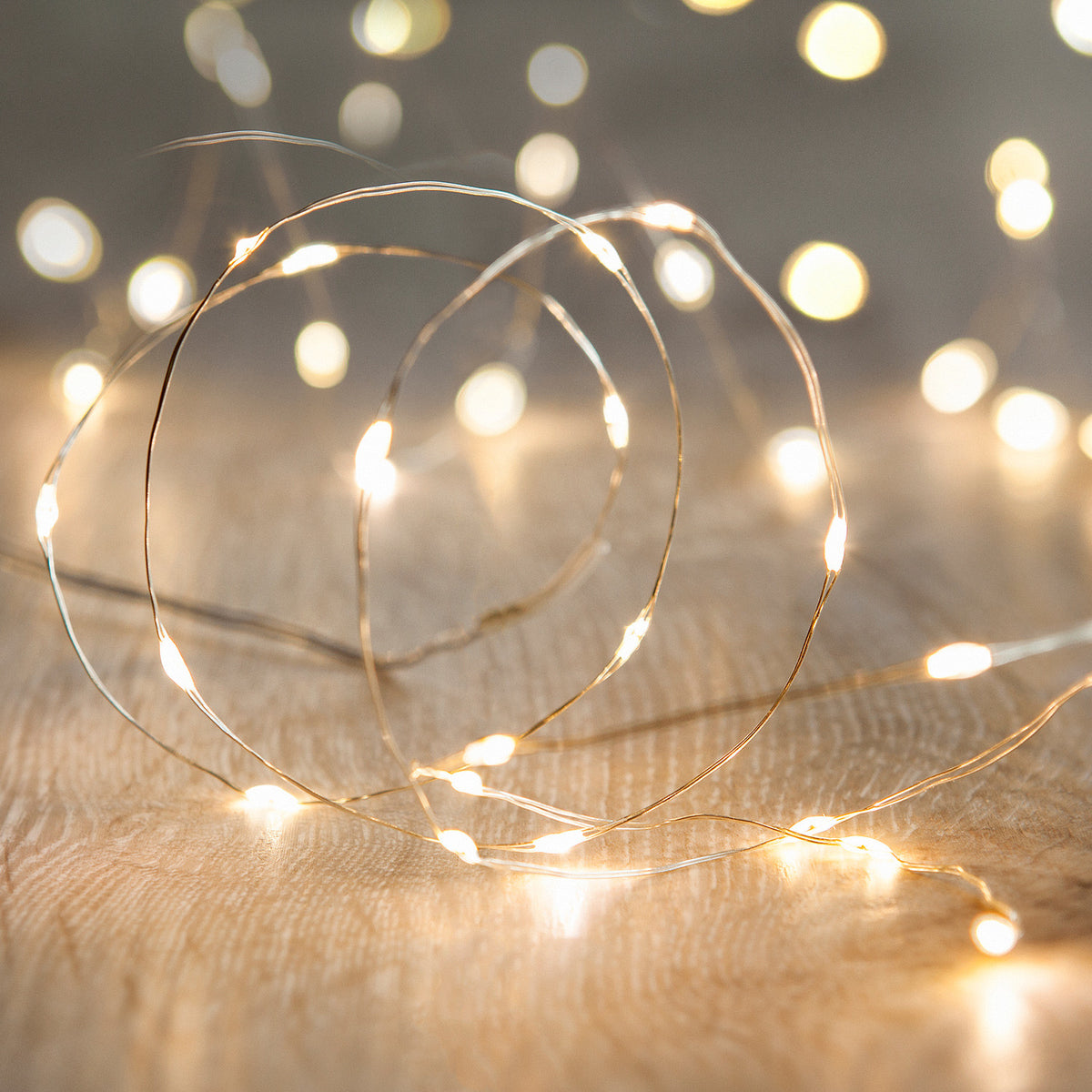 Nahaufnahme einer warmweißen LED-Mikrolichterkette auf hellem Holz mit unscharfen Lichtern im Hintergrund