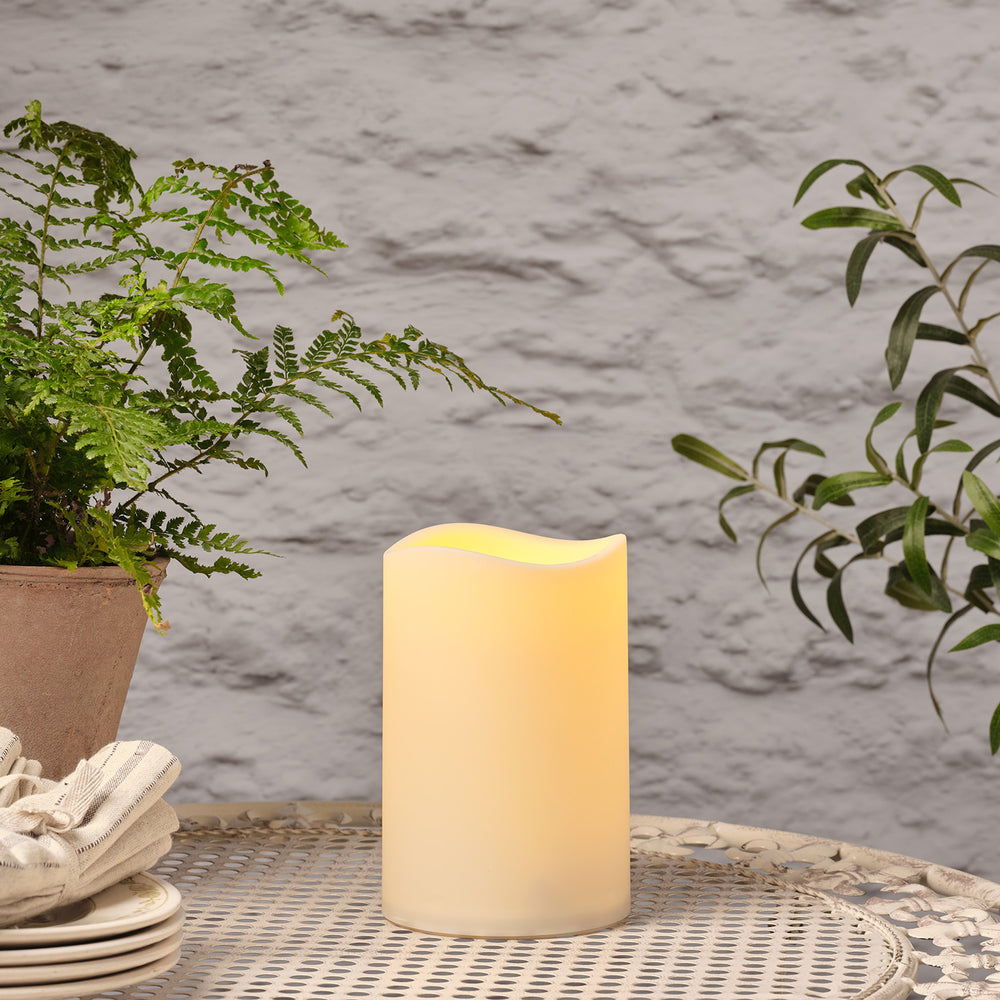 Ausgeschaltete LED Outdoor Kerze auf Gartentisch mit Pflanzen im Hintergrund
