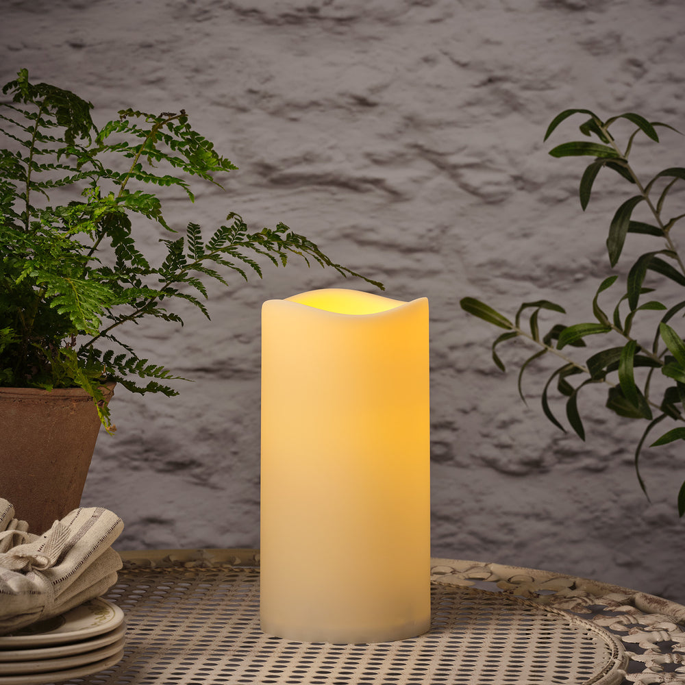 Leuchtende LED Outdoor Kerze auf Metalltisch mit Pflanzen im Hintergrund