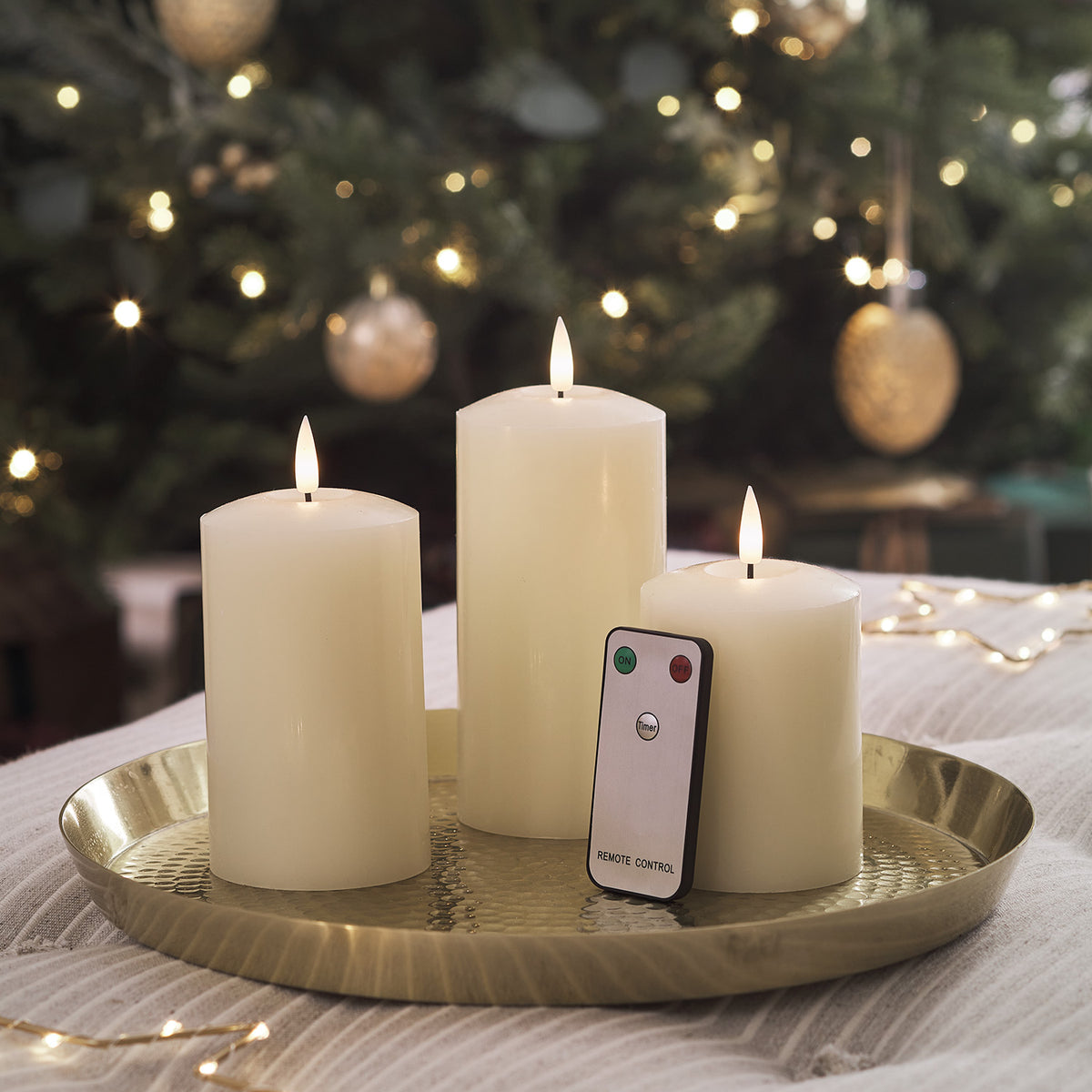 Drei LED-Kerzen auf einem dunklen Tablett vor weihnachtlicher Dekoration
