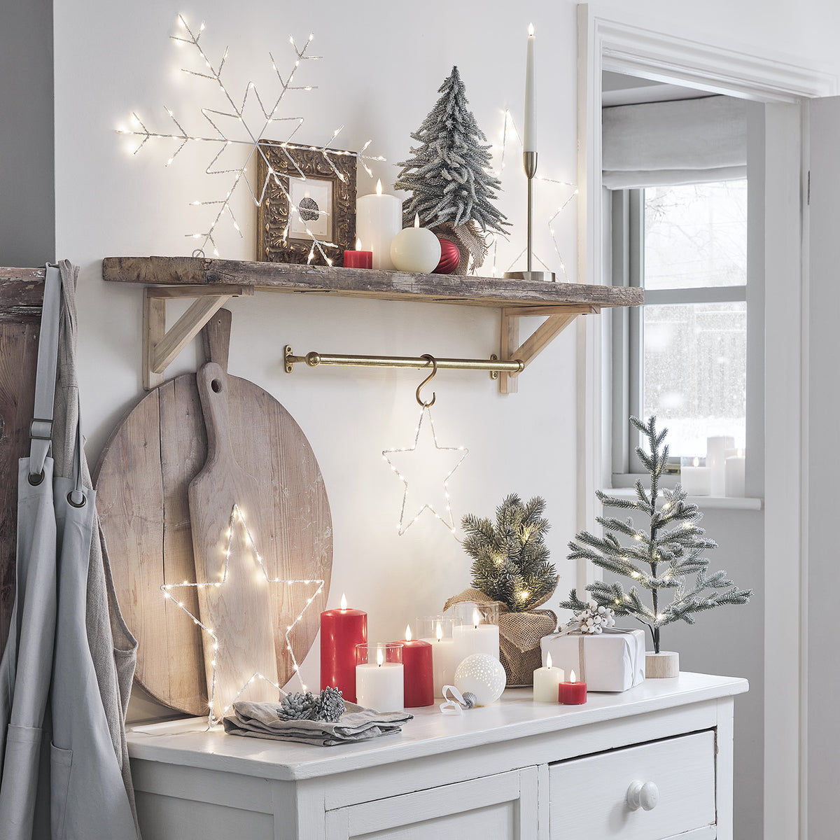 Weihnachtliche Dekoration mit roten LED-Kerzen, Lichterstern und kleinen Tannenbäumen auf Kommode