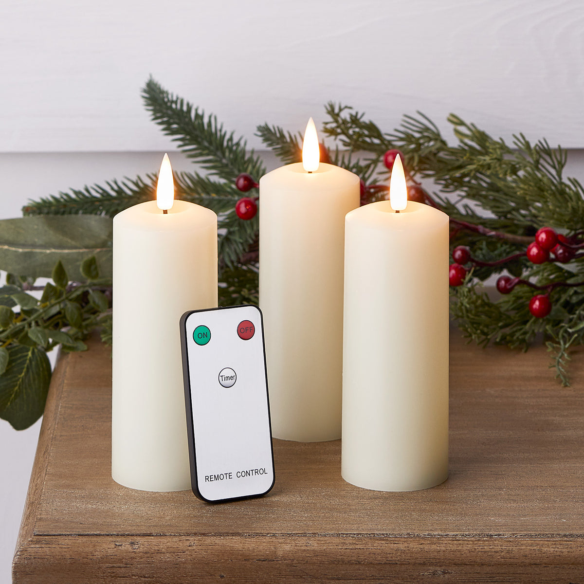 Drei schmale LED Stumpenkerzen mit Fernbedienung auf Holztisch vor grüner Dekoration