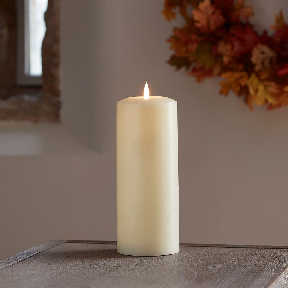TruGlow LED Stumpenkerze mit Fernbedienung auf Holzfläche vor herbstlicher Dekoration