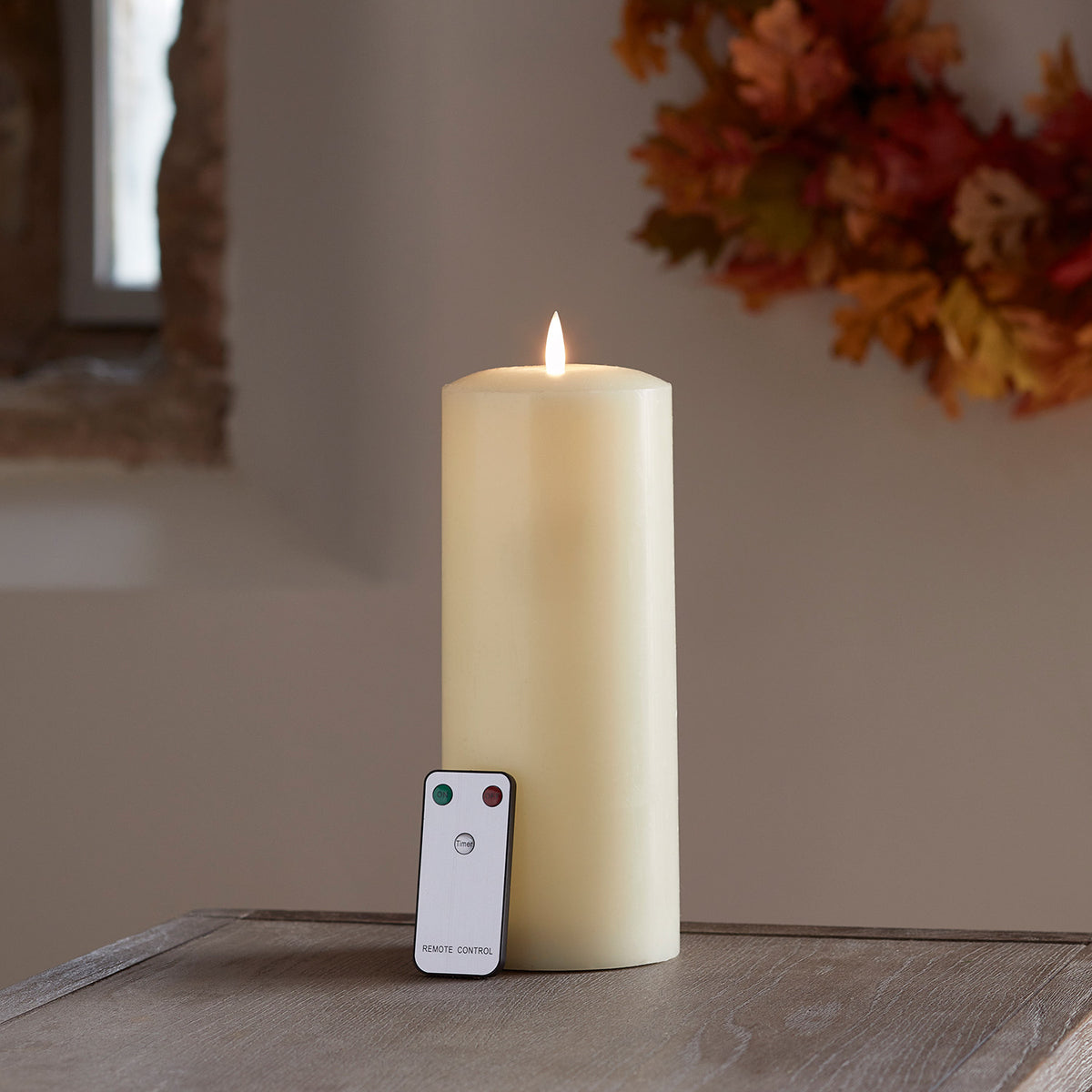TruGlow LED Stumpenkerze mit Fernbedienung auf Holzfläche vor herbstlicher Dekoration