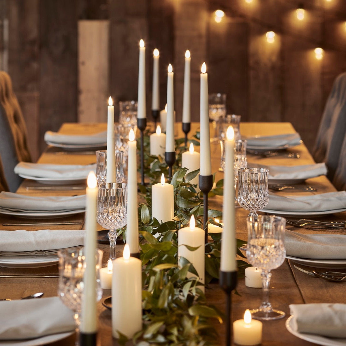 Elegante gedeckte Tafel mit brennenden LED Stabkerzen und Glasgeschirr in rustikalem Ambiente