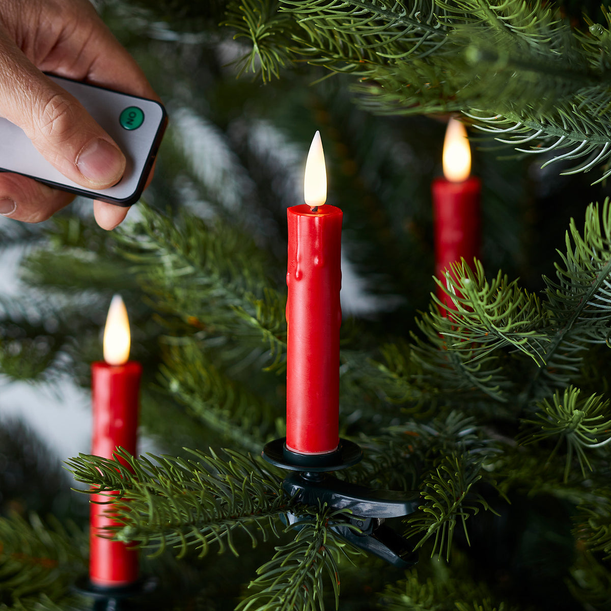 Hand mit Fernbedienung steuert rote LED Baumkerze an Tannenzweig mit Clip