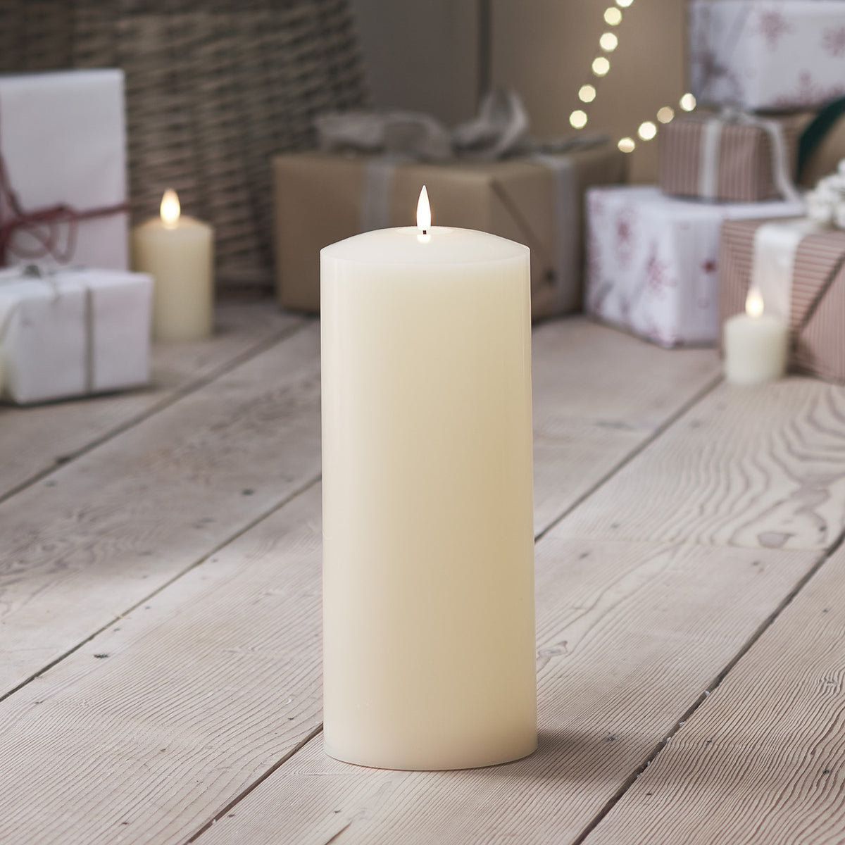 LED Stumpenkerze auf hellem Holzboden umgeben von Geschenken und Lichterkette im Hintergrund