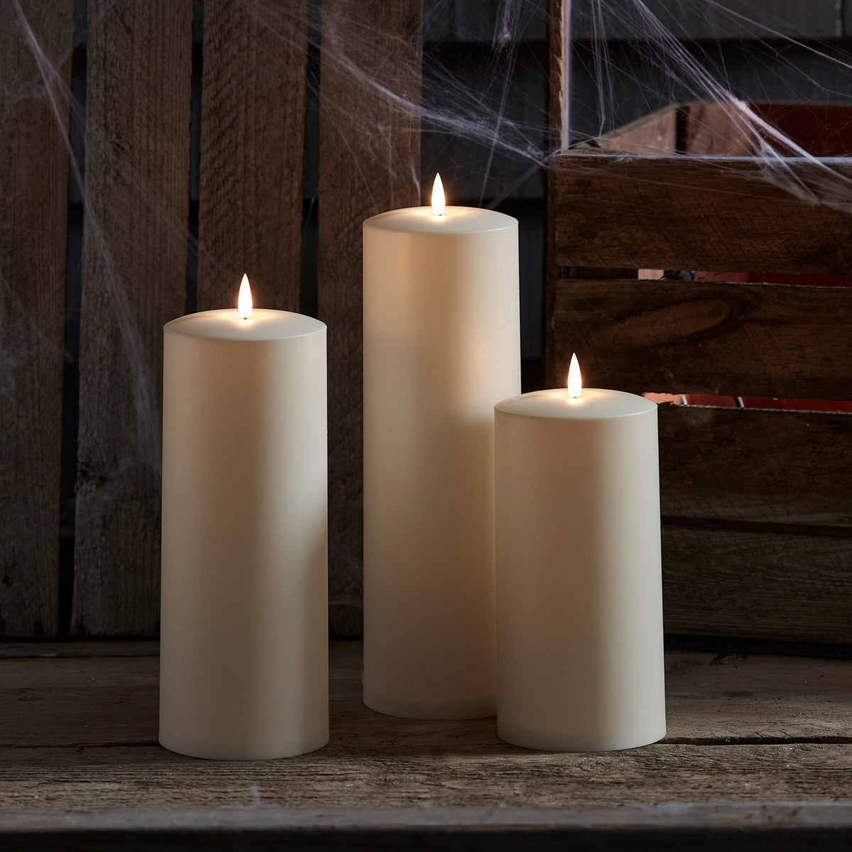 Drei brennende LED-Kerzen vor Holzwand mit Spinnweben dekoriert