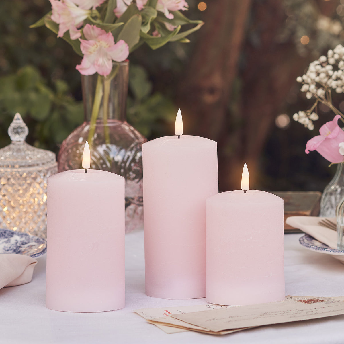 Drei rosa LED Stumpenkerzen mit Fernbedienung und Osterdeko auf weißem Tisch