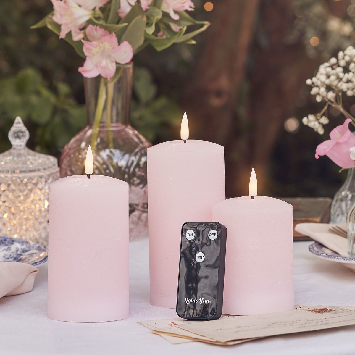 Drei rosa LED Stumpenkerzen mit Fernbedienung auf Tisch mit Osterdeko und Briefen