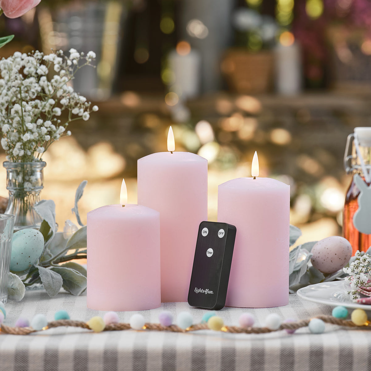 Drei rosa LED Stumpenkerzen mit Fernbedienung auf Gartentisch mit Osterdeko
