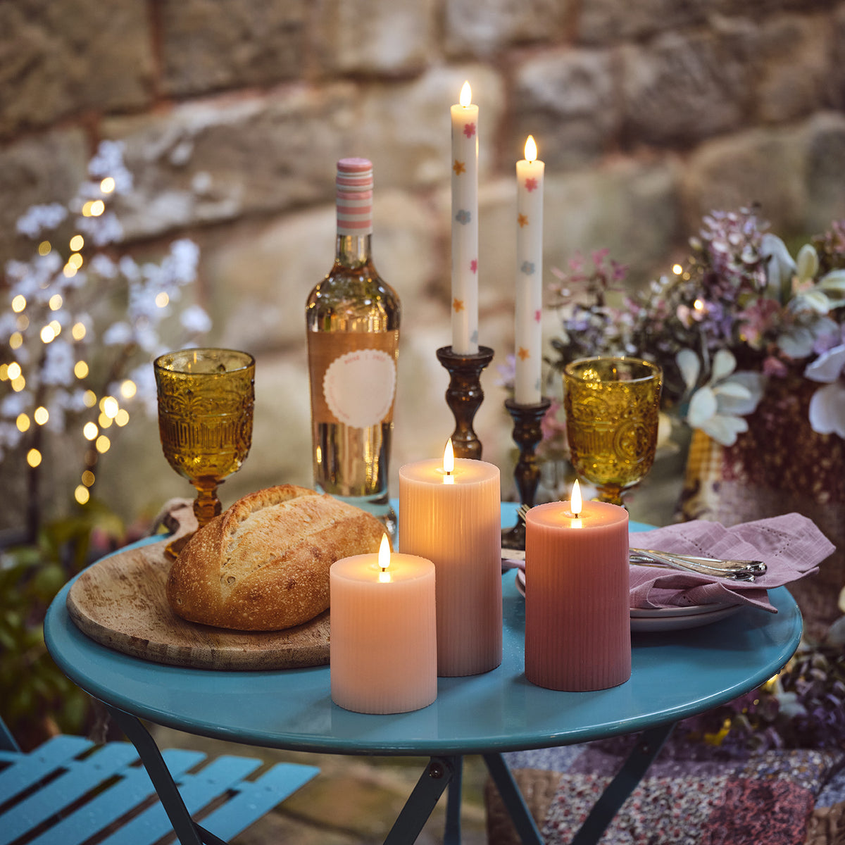 LED-Kerzen in Rosa- und Pastelltönen mit Osterdeko auf blauem Gartentisch