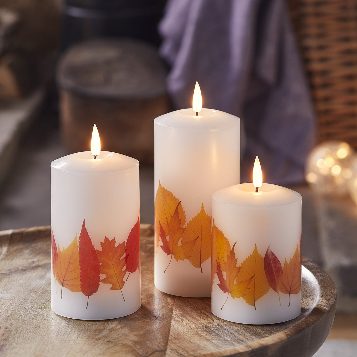 Drei TruGlow LED Kerzen mit Herbstblättern in verschiedenen Höhen auf einem Holztisch