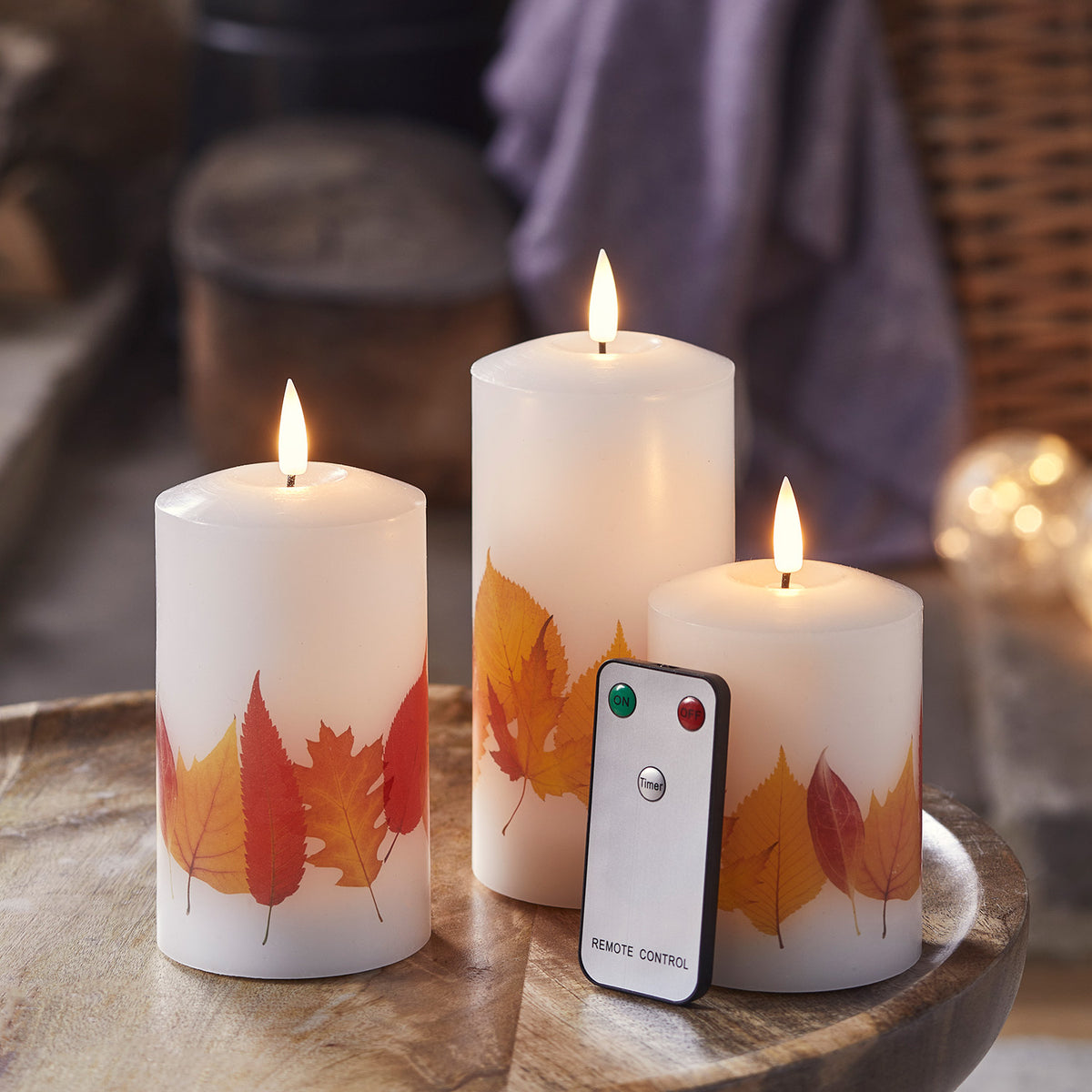 Drei leuchtende LED Kerzen mit Herbstblättern und Fernbedienung auf Holztisch
