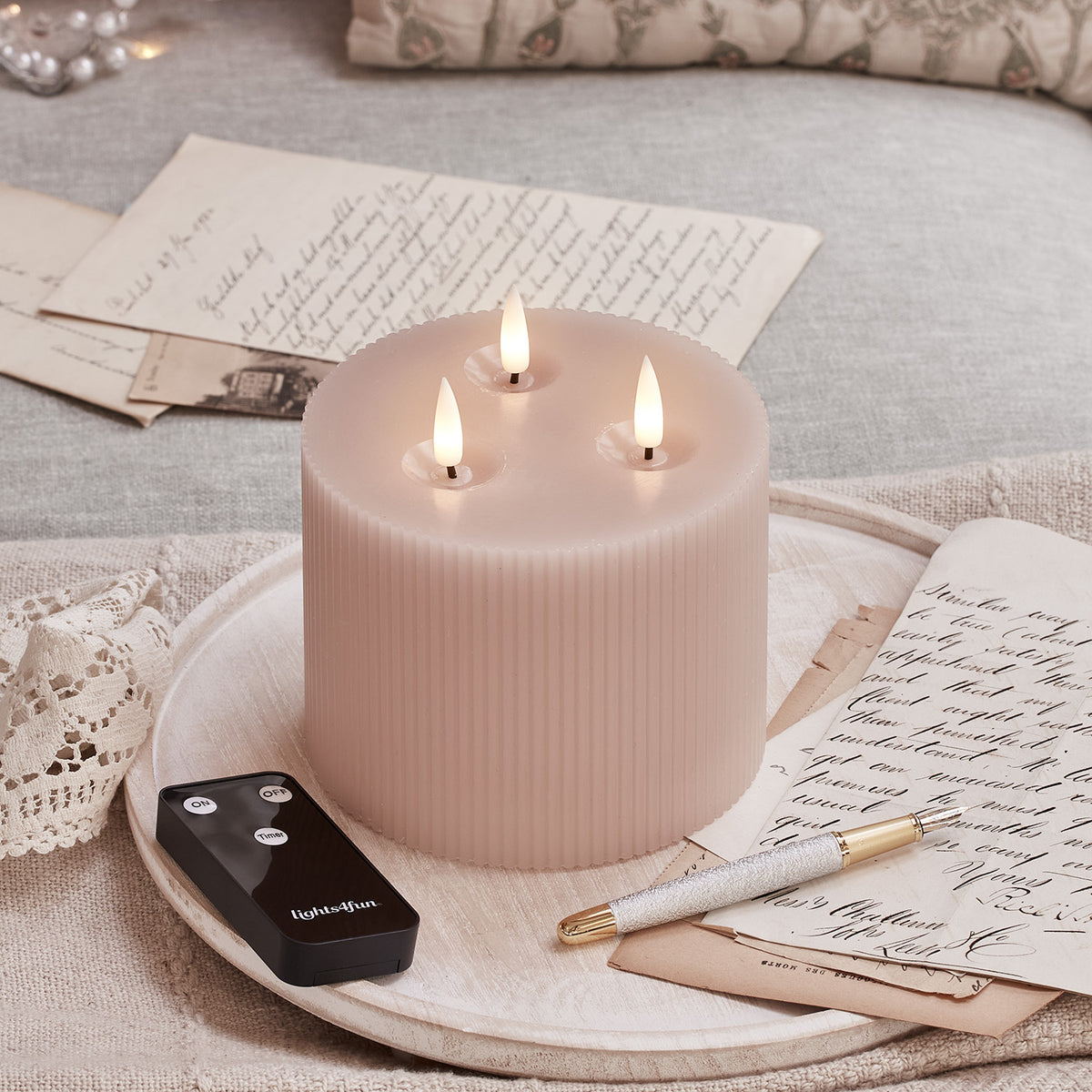 Geriffelte rosa LED-Kerze mit drei Dochten und Fernbedienung auf Holztablett mit Briefen und Stift