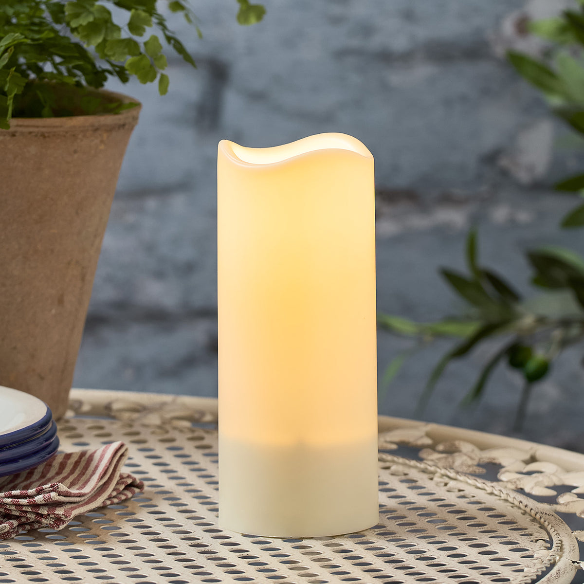 Große Solarkerze mit warmem Licht auf einem Metalltisch, umgeben von Pflanzen