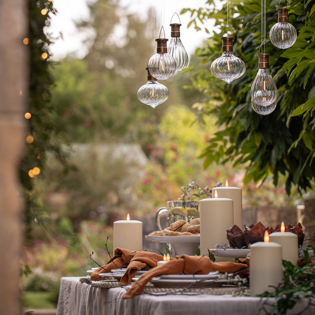 Beleuchteter Gartentisch mit TruGlow Solarkerzen und hängenden Glaslampen im Garten