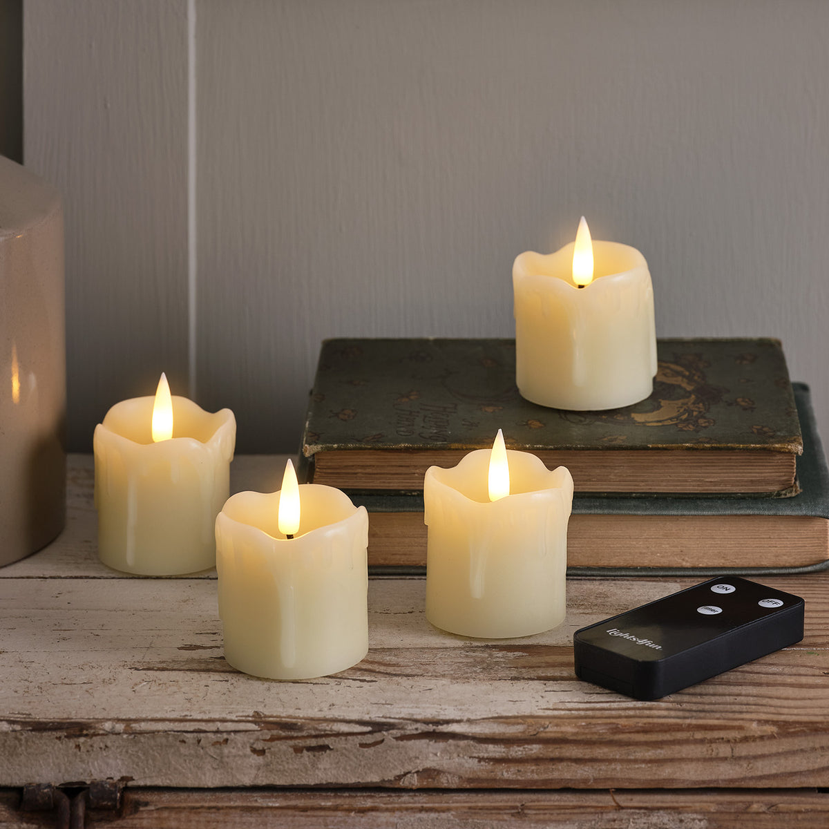 Vier LED-Teelichter aus Wachs mit Fernbedienung auf Holz, eines auf alten Büchern
