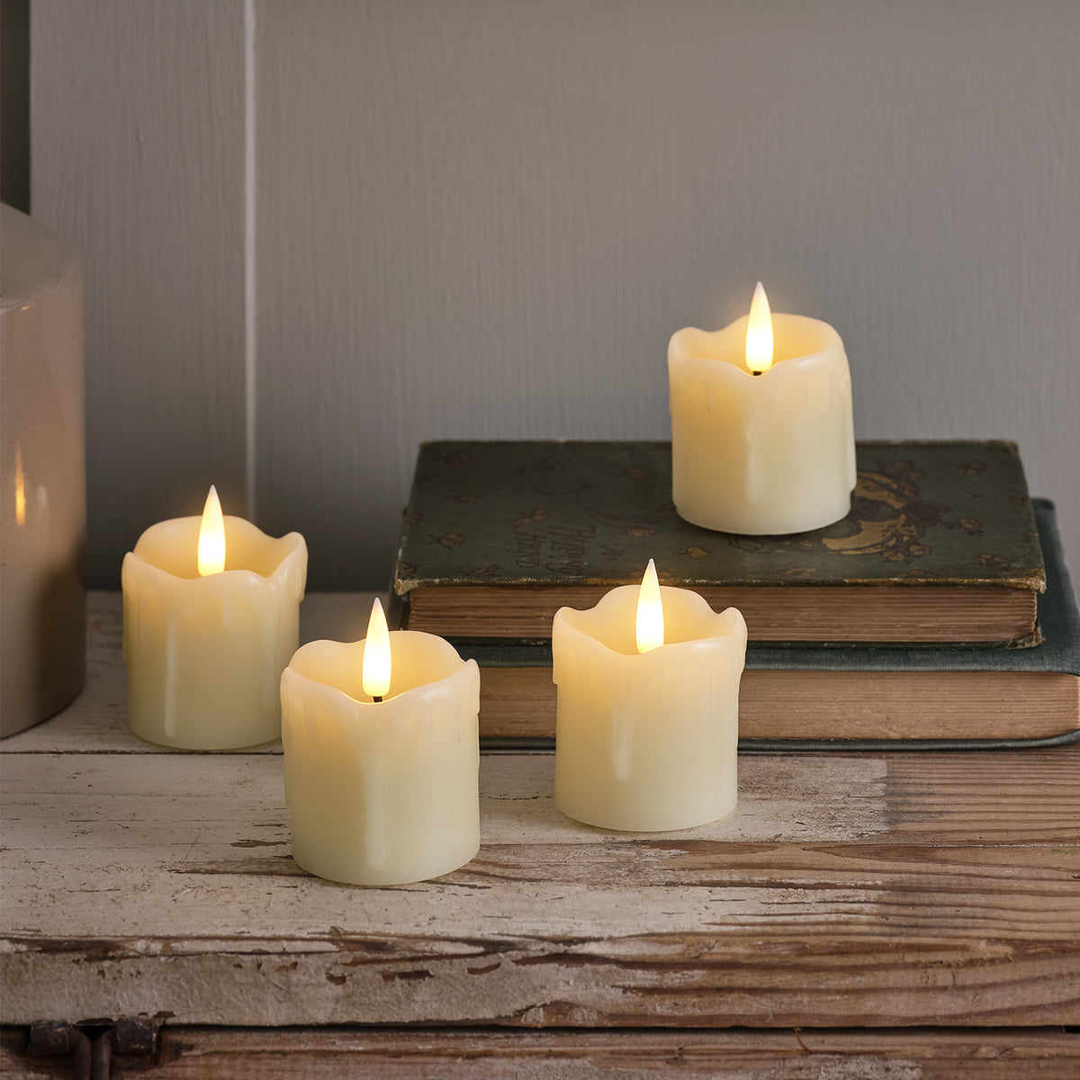 Drei LED-Teelichter aus Echtwachs auf Holzfläche, eines auf alten Büchern mit flackerndem Licht