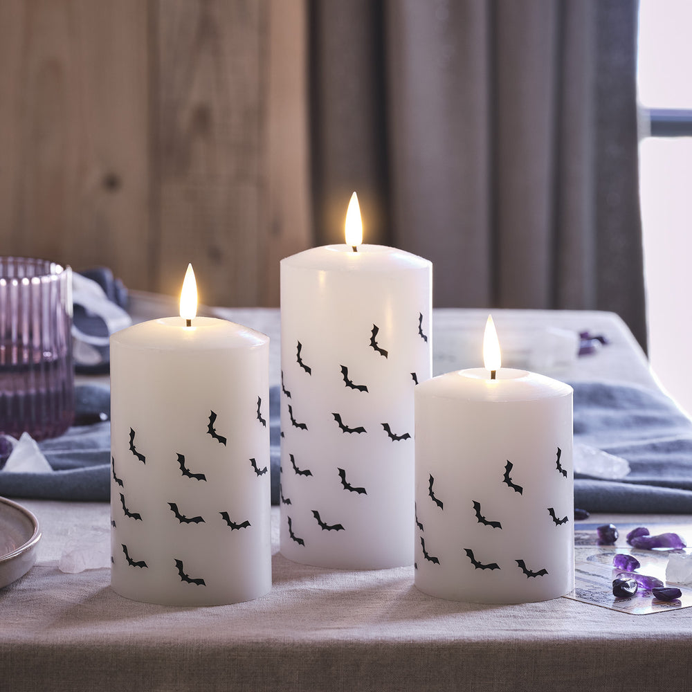 Drei weiße LED Stumpenkerzen mit schwarzen Fledermausmotiven auf einem Tisch