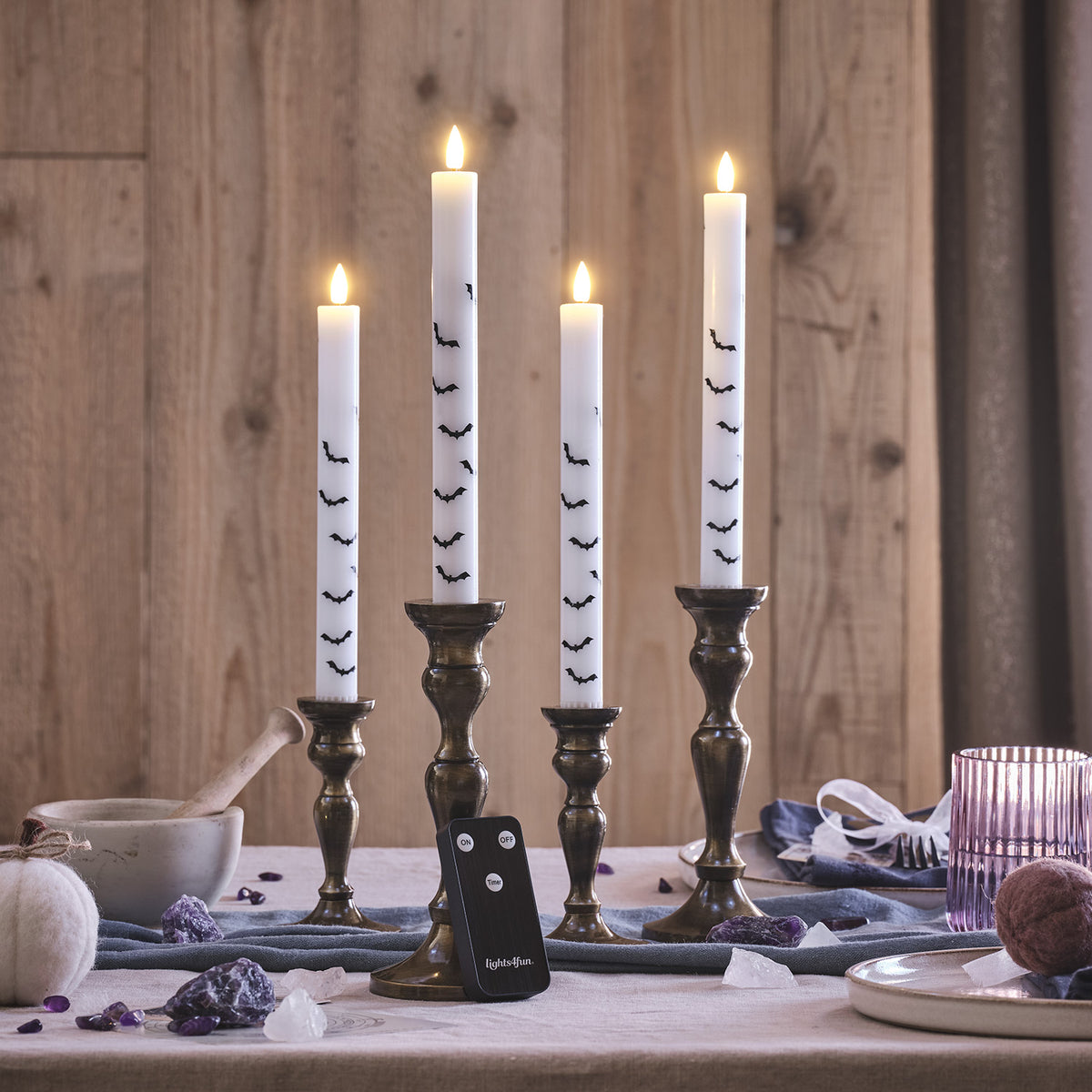 Vier weiße LED Stabkerzen mit Fledermaus-Motiv in Messing-Kerzenhaltern und Fernbedienung auf Tisch