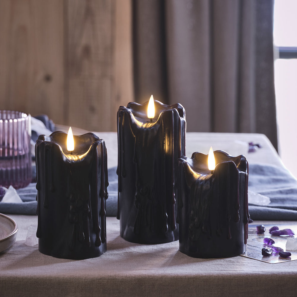 Drei schwarze LED Stumpenkerzen mit Wachstropfen und warmweiß flackernder Flamme auf Tisch