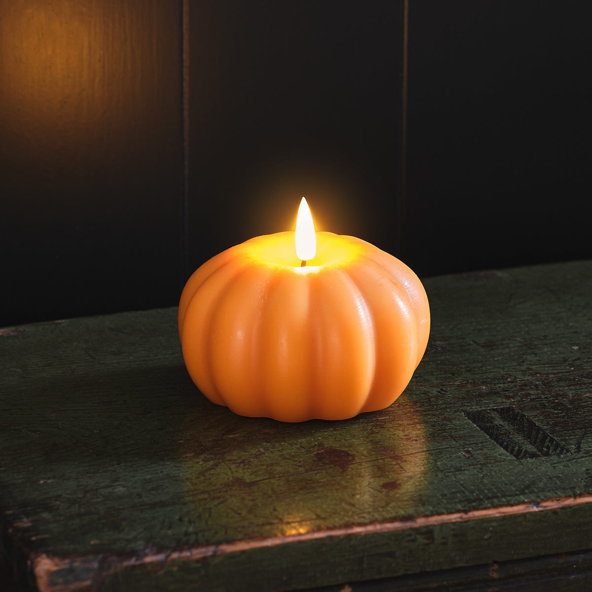 Leuchtende orangefarbene LED-Kürbiskerze auf dunklem Holztisch vor schwarzem Hintergrund