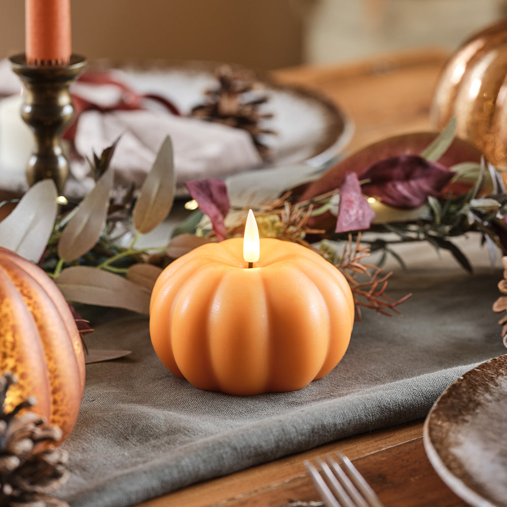 Orangefarbene LED-Kerze in Kürbisform auf grauem Stoff mit herbstlicher Tischdeko