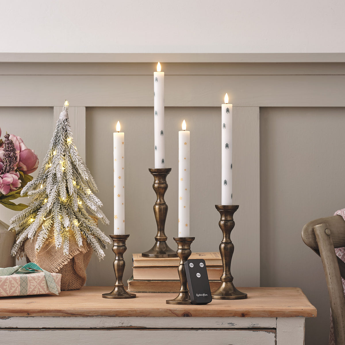 Vier LED Stabkerzen mit Weihnachtsmotiven in Messinghaltern und Fernbedienung auf Holztisch