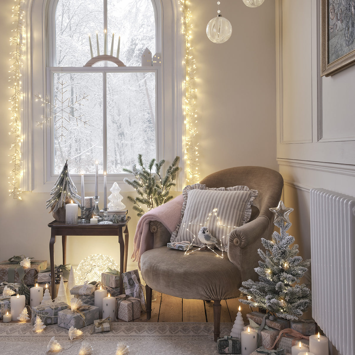Gemütliche Ecke mit LED Stabkerzen, Weihnachtsdeko und Sessel vor Fenster mit Schneelandschaft