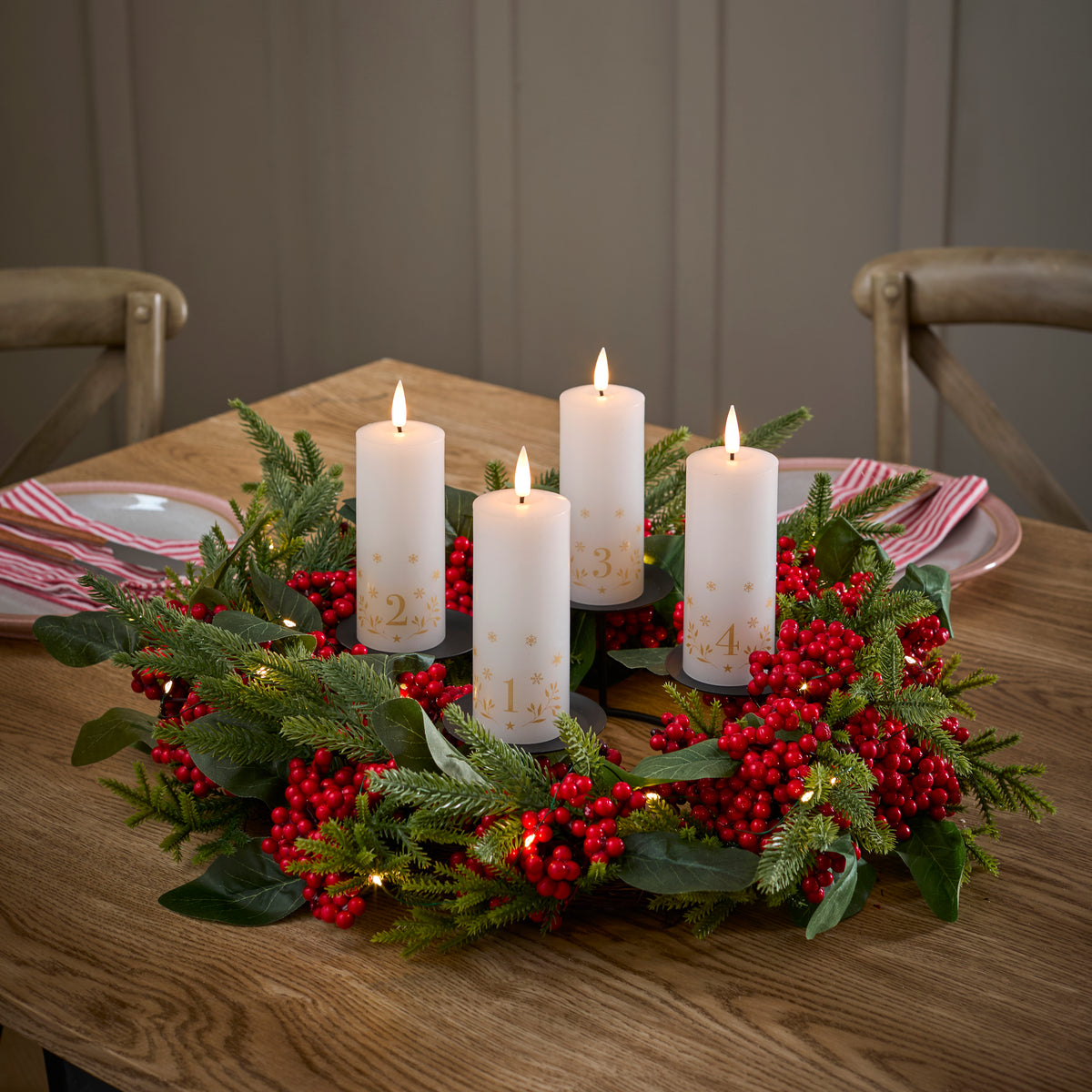 LED Adventskerzen mit Zahlen in einem Adventskranz aus Tannenzweigen und roten Beeren auf Esstisch